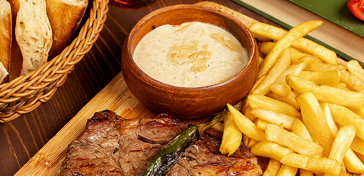 Beef steak with french fries, sour cream mayonnaise sauce and herbs on wooden plate. image